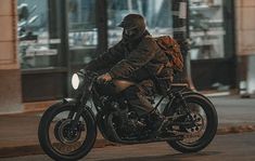 a man riding on the back of a motorcycle down a street next to a tall building