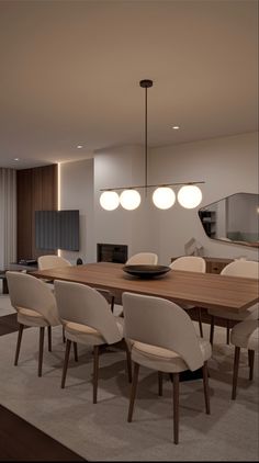 the dining room table is surrounded by white chairs and modern lighting fixtures, along with an area rug that matches the hardwood flooring