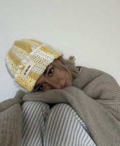 a woman wrapped up in a blanket and wearing a knitted hat with her face peeking out