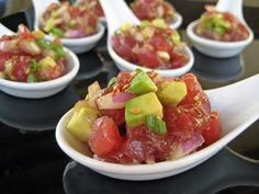 several small white bowls filled with food on top of a black counter topped with spoons