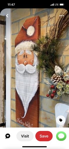 a wooden sign with a santa clause on it next to a brick wall and potted plants