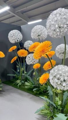 an arrangement of white and yellow flowers on display in a room with gray walls,