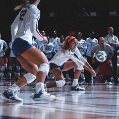 two women playing volleyball on a court with people watching from the sidelines behind them