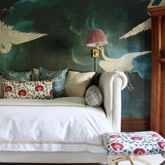 a white bed sitting in a bedroom next to a wall covered in birds and clouds