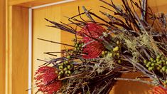 a wreath with red flowers and green berries hanging on a wooden door frame in front of a wood paneled wall