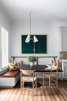 a dining room table with two chairs and a bench in front of a painting on the wall