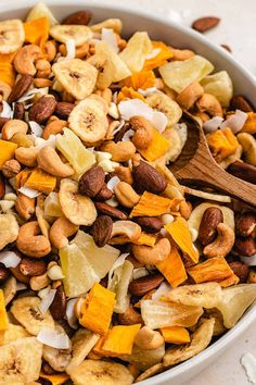 a bowl filled with nuts and fruit on top of a white countertop next to a wooden spoon