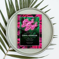 a pink and green tropical bachelor party card on a metal tray with palm leaves around it