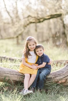 two children sitting on a log in the grass with their arms around each other and smiling