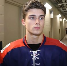 a young man in an orange and blue hockey jersey is looking at the camera while standing in a hallway