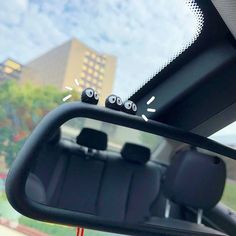 the interior of a car with three eyes on it's side mirror and buildings in the background