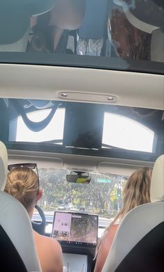 two women sitting in the back seat of a car looking at a laptop computer screen