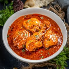 a white bowl filled with meat covered in sauce and garnished with parsley