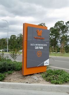 an orange and gray sign sitting on the side of a road next to a parking lot