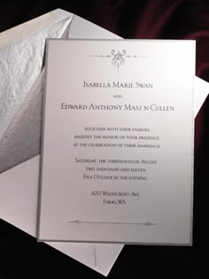 a white wedding card with an ornate design on the front and back, sitting on a black background