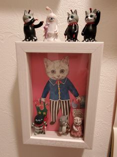 a white frame with some cats in it on top of a wall next to a cat figurine