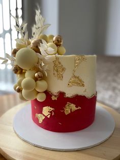 a red and white cake with gold decorations on top is sitting on a wooden table