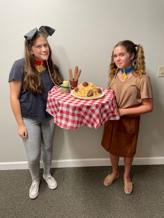 two girls standing next to each other in front of a table with food on it