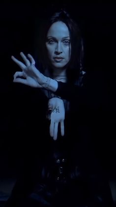 a woman sitting in the dark holding her hands out with one hand and two fingers extended