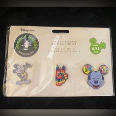 three disney pins in plastic packaging on a black table with white border and mickey mouse stickers