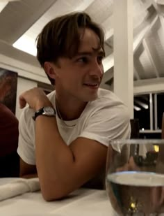 two young men sitting at a table with wine glasses in front of them, smiling