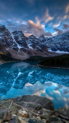 the mountains are covered in snow and clouds as they rise above a blue mountain lake