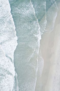 an aerial view of the ocean and beach with waves crashing on it's shore