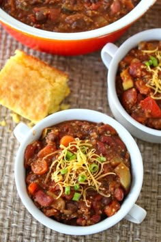 two white bowls filled with chili and cornbreads next to a bowl of bread