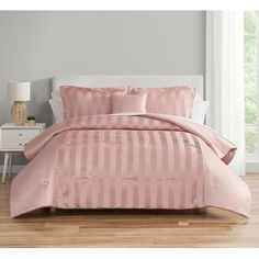 a bed with pink comforter and pillows in a white room next to a window