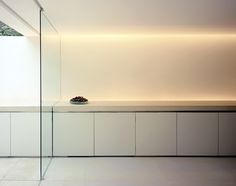 an empty white room with a bowl on the counter and glass walls in front of it