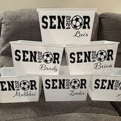 six white baskets with black lettering on them sitting on a couch in front of a gray chair