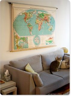 a cat sitting on top of a gray couch in front of a large world map