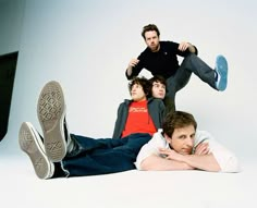 three young men sitting on the floor with their feet up and one man standing behind them