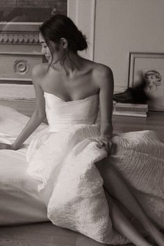 a woman in a white dress sitting on a bed