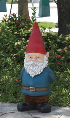 a gnome statue sitting on top of a stone slab in front of some bushes and trees