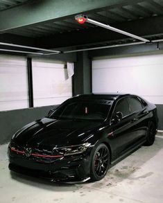 a black car parked in a parking garage next to two red lights on the ceiling