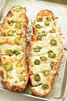 two pieces of bread with cheese and green olives on it sitting on a baking sheet