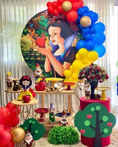 a table with balloons and other decorations on it in front of a wall mural that has snow white holding an apple