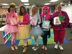 four girls dressed in costumes holding books and posing for the camera with one girl wearing a tiara