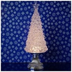 a glass christmas tree on a table with snowflakes in the backgroud