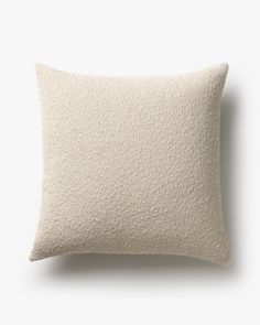 a white pillow with a textured design on the front and back, sitting against a white wall