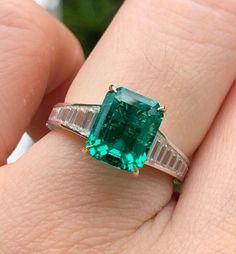 an emerald and diamond ring on someone's finger with two baguettes in the band