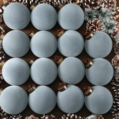 twelve blue christmas balls with gold bows and pine cones on a wooden table surrounded by pine cones