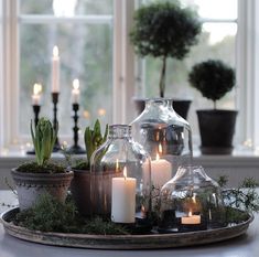 candles are lit in glass vases on a tray with succulents and moss