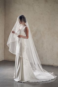 a woman in a white wedding dress with a veil on her head is looking down at the floor