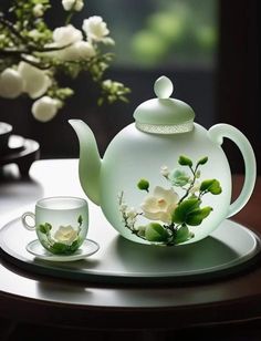 a glass teapot with flowers on it next to a cup and saucer