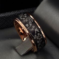 a black and gold wedding ring with flowers on the inside is sitting on a gray surface