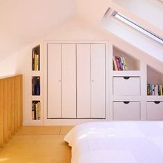 a bed sitting under a window in a bedroom next to a book shelf and cupboards