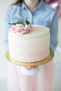 a woman holding a white cake with pink flowers on top