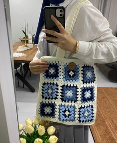 a woman holding a cell phone in front of a crocheted bag with flowers